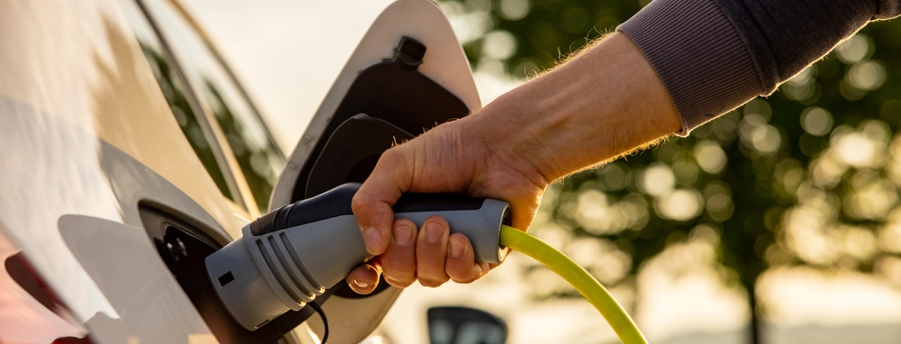 Nahaufnahme einer Hand, die gerade den Stecker zum Aufladen eines E-Autos in Auto einsteckt