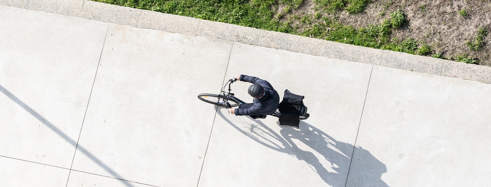 Ein Fahrradfahrer von oben fährt auf einem Gehweg in der Sonne