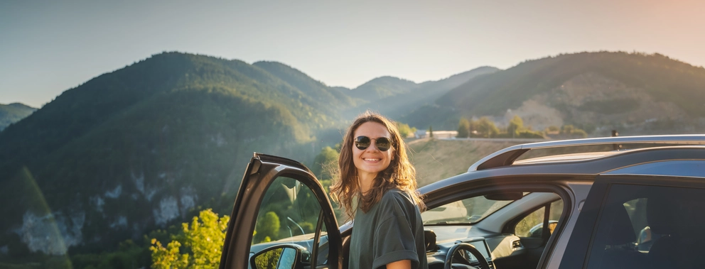 Eine Frau steigt aus einem Auto aus, im Hintergrund is eine Berglandschaft zu sehen